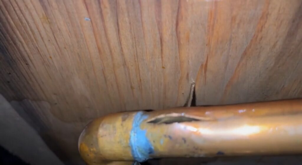 Copper water pipe split open from freezing under a wood subfloor