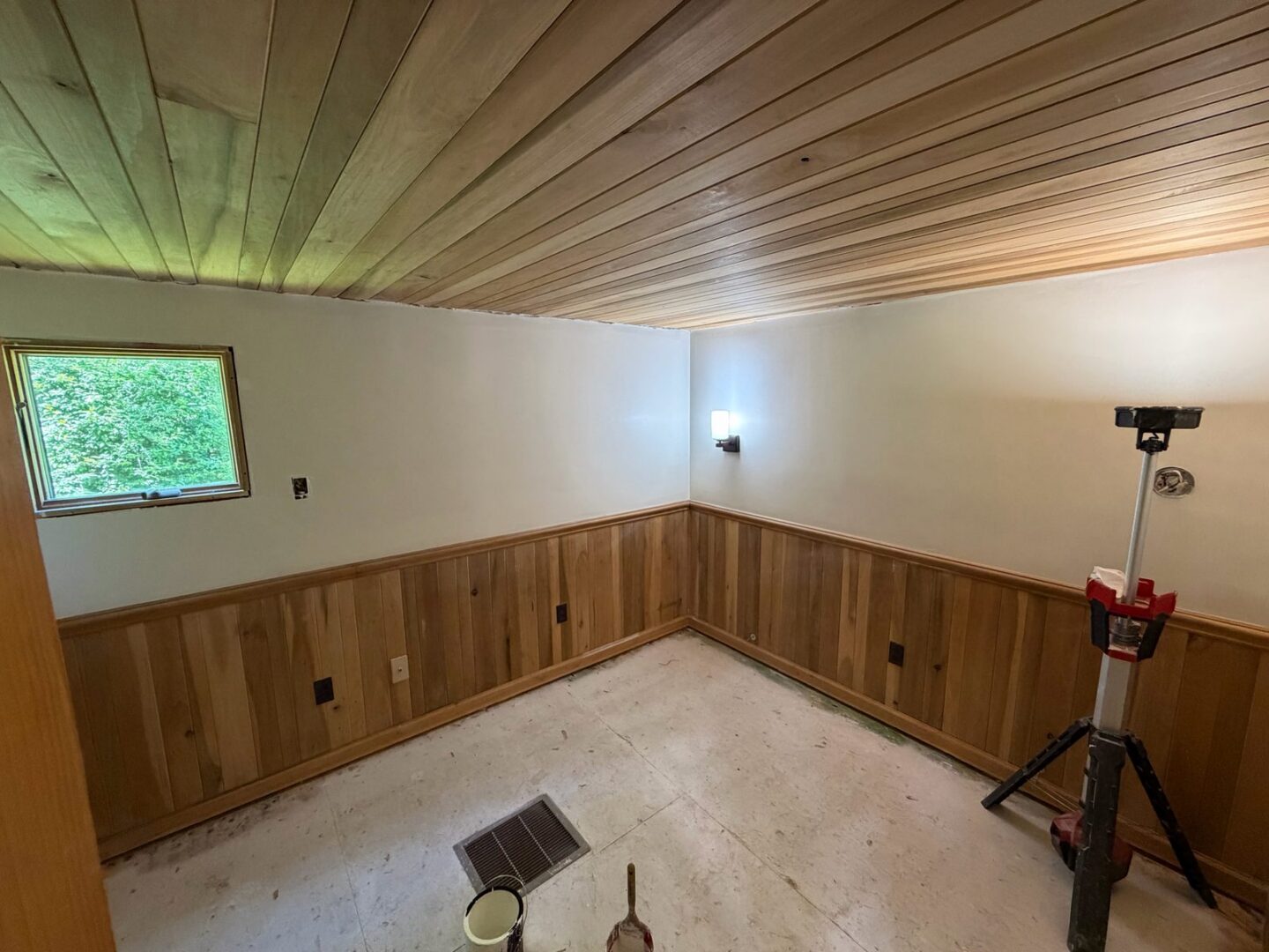 Basement room with a wood plank ceiling, wood wainscot and a work light