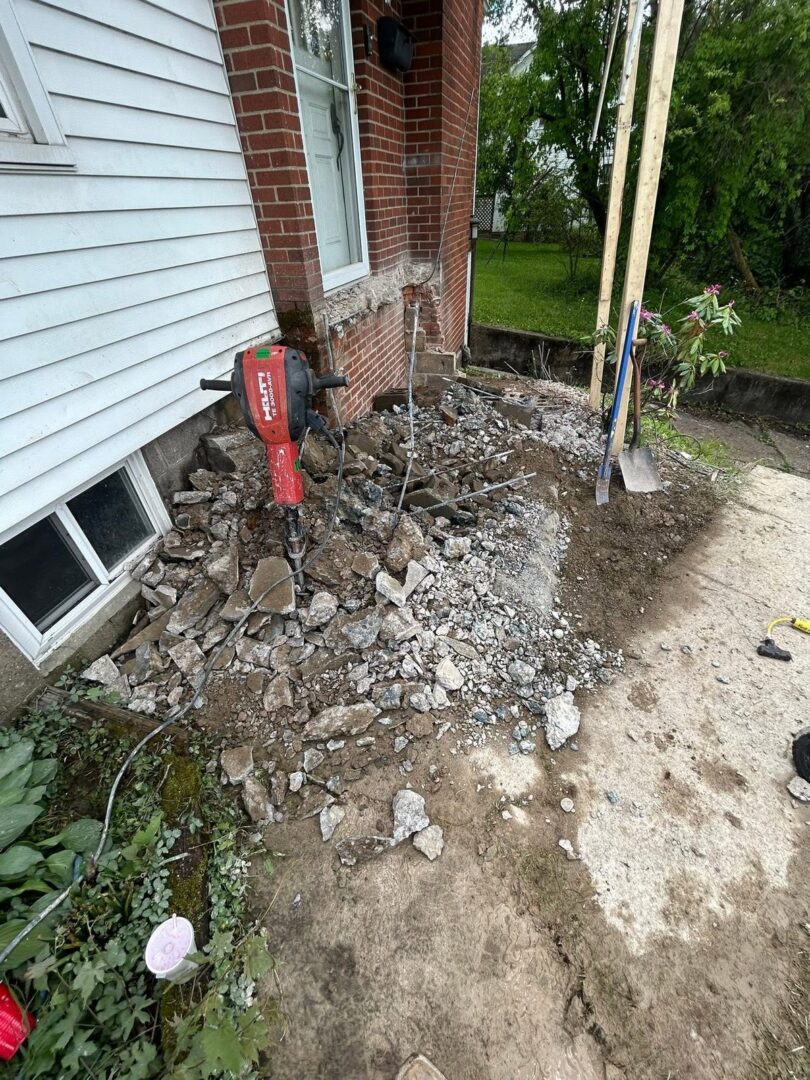 Concrete steps broken out with a jackhammer beside a brick and siding house